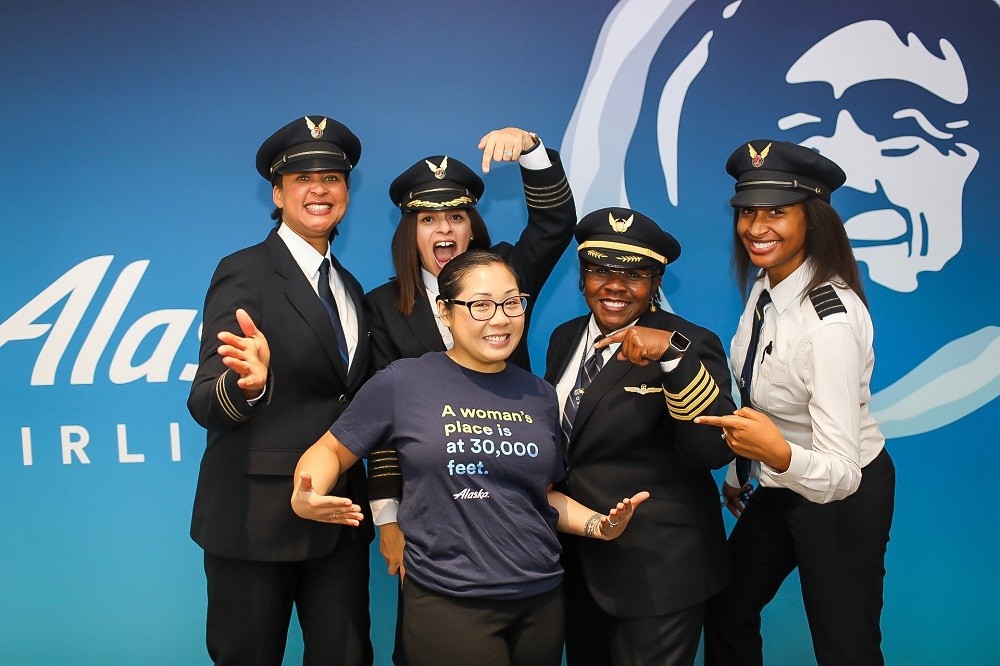 Five women pilots and representatives from Alaska Airlines and Sisters of the Skies pose for a photo, highlighting the partnership to promote diversity in aviation careers.