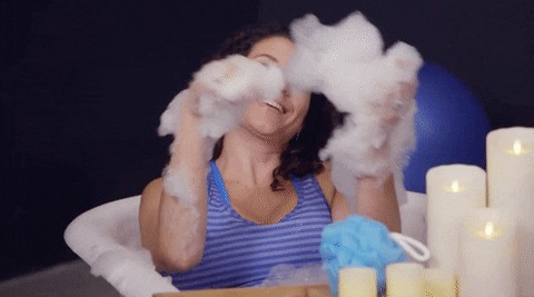 Person playfully enjoying a bubble bath, highlighting the cliché of traditional self-care