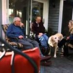 Three people sitting on porch with a dog