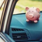 A piggy bank sits perched on the dash console of a car