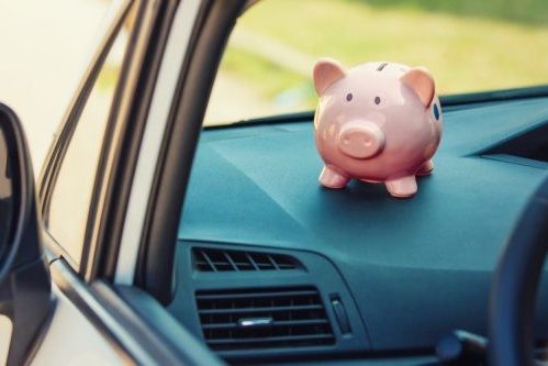 A piggy bank sits perched on the dash console of a car