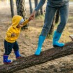 Adult caregiver and child walking on logs in a forest, representing outdoor activities in therapeutic care