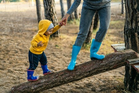 Adult caregiver and child walking on logs in a forest, representing outdoor activities in therapeutic care