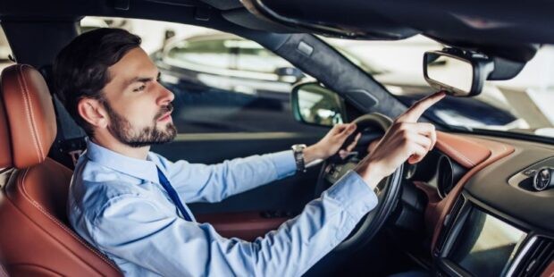 Man programming HomeLink buttons in car rearview mirror for garage door opener.